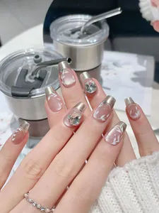 Detailed view of silver French tip press-on nails with leaf art and sparkling rhinestones
