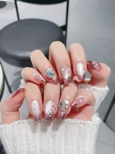 Detail of pink gradient press-on nails with leaf pattern, rhinestones, and metallic glitter