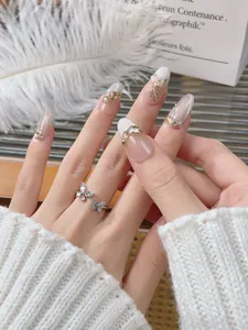 Nahaufnahme von Mandel-Kunstnägeln mit champagnerfarbenem Schmetterling und Strass