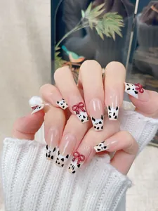 Detail of French milk cow pattern press-on nails with 3D red bows and coffin shape