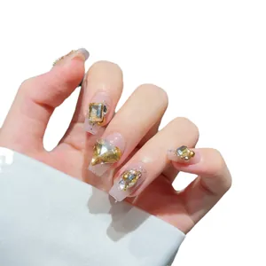 Handmade press-on nails with luxury rhinestones and gold heart accents on nude coffin shape