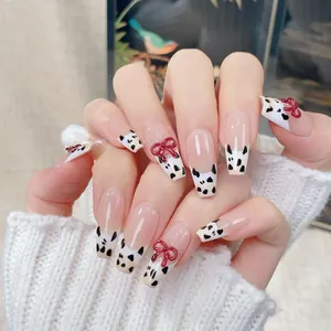 French cow print press-on nails with 3D red bows on a cozy white knit background