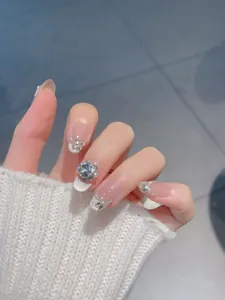 Detail of nude press-on nails with silver French tips, pearls, and zircon butterfly charms