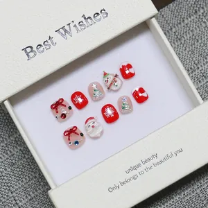 Handmade Christmas press-on nails featuring red snowman and tree motifs in a gift box