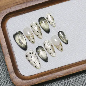 Faux ongles œil de chat vert foncé avec perles et étoiles dorées sur plateau bois