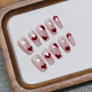 Sparkling pink cat-eye press-on nails with red 3D hearts on a wooden display tray