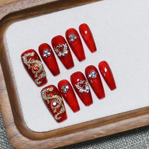 Handmade red press-on nails with golden dragon and crown charms on wooden tray