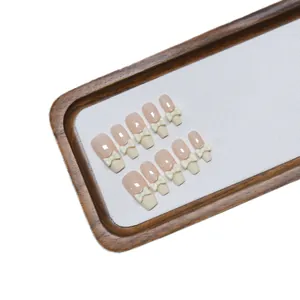 Press-on nails set featuring nude French tips with 3D white resin bows on a wooden tray