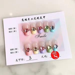 Détail de faux ongles macaron avec strass cœur 3D sur un panneau d'affichage blanc