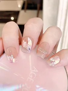Detail of pink mermaid-style press-on nails with pearls and gold chain accents
