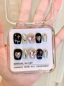 Close-up of handmade black and pink press-on nails with 3D hearts and rhinestones in a box