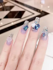 Vista macro de dijes de rosas 3D y diamantes azules en uñas postizas tipo press-on