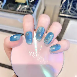 Faux ongles œil-de-chat bleus avec paillettes étoiles et strass tenus sur boîte rose