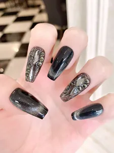 Macro detail of long coffin press-on nails with black cat-eye finish and luxury gemstones