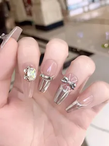 Macro shot of silver metallic press-on nails with shiny rhinestones and bow accents