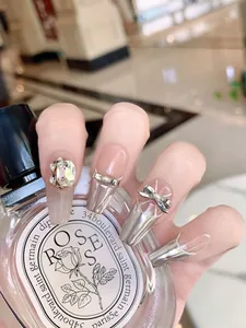 Detail of luxury press-on nails featuring rhinestones, silver bows and French tips