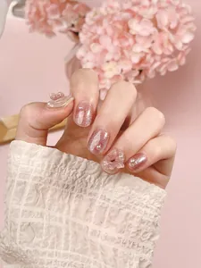 Detailed view of pink cat eye press-on nails with 3D butterfly bows and pearls