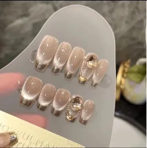 Nahaufnahme der Nude-Cat-Eye-Nägel mit goldenen Metallspitzen und Kristallakzenten