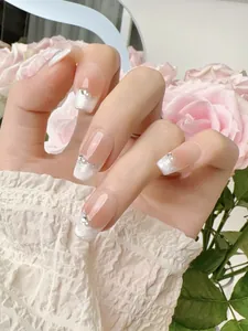 Detail of square-oval press-on nails with French blush design, pearls, and rhinestones