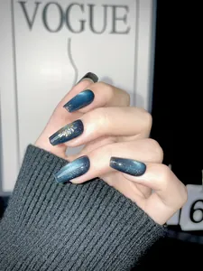 Detail of blue cat eye press-on nails with golden fireworks design and long coffin shape