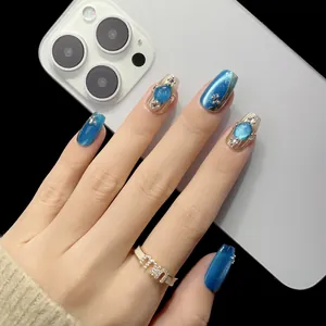 Blaue Cat-Eye Kunstnägel mit Edelstein-Akzenten und Goldfolie auf weißem Grund