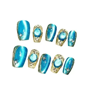 Blaue Katzenaugen-Nagel-Set mit Goldrelief und Kristallen auf weißem Grund