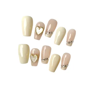 Faux ongles faits main en crème et rose nude avec cœurs dorés et strass brillants