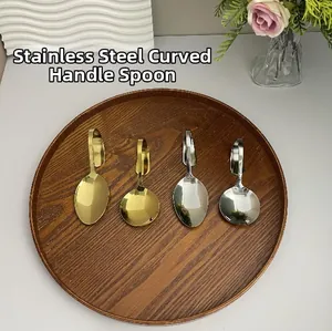 Gold- und silberfarbene Edelstahllöffel mit gebogenem Griff auf einem Holztablett mit Blumen