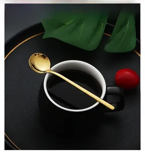 Top view of a gold long-handled stainless steel round spoon next to a black coffee cup