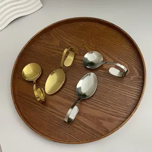 Kreative Edelstahllöffel mit gebogenem Griff in Gold und Silber auf einem Holztablett