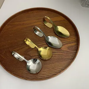 Edelstahllöffel-Set mit gebogenem Griff in Gold und Silber auf einem Holztablett