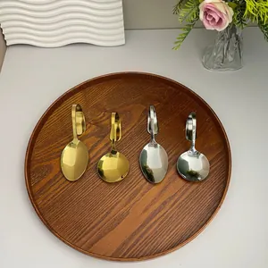Detailaufnahme der gebogenen Edelstahllöffel in Gold und Silber auf einem Holztablett