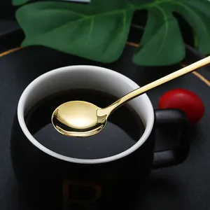 Golden 304 stainless steel long handle round coffee spoon leaning on a black ceramic cup