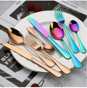 Set di posate in acciaio inossidabile arcobaleno e oro rosa su un piatto bianco