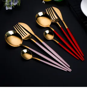 Close-up of golden stainless steel cutlery with red and purple handles on dark background