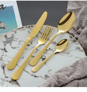 Détail de couverts dorés en acier inoxydable sur assiette en marbre et lin gris