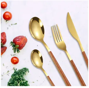 Close-up of gold stainless steel cutlery set with wooden handles on marble surface
