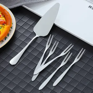 Polished stainless steel cake server and dessert fork set on a black grid background