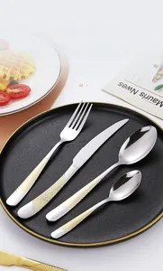 Detail view of silver stainless steel cutlery set with gold grid handles on a black plate