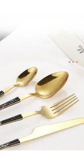 Close-up of gold stainless steel cutlery set with black marble texture handles on ceramic