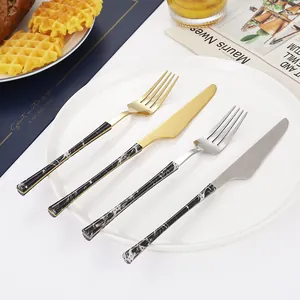 4-piece marble handle stainless steel cutlery set with gold finish on white plate