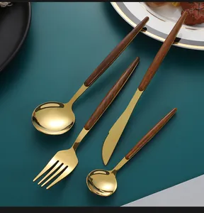 Détail de couverts 4 pièces en inox doré avec manches imitation bois sur fond vert foncé
