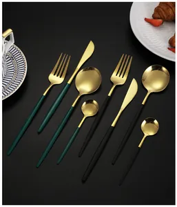 Gros plan de couverts dorés en acier inoxydable avec manches noir mat et vert sur la table
