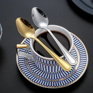 Polished gold and silver stainless steel coffee spoons on blue striped ceramic mug