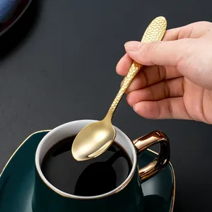 Cuillère à café en acier inoxydable doré martelé tenue devant une tasse verte