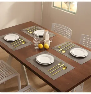 Modern gold cutlery set with deep grey woven placemats on a wooden dining table