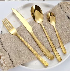 Détail d'un ensemble de 4 couverts en acier inoxydable doré martelé sur assiette blanche