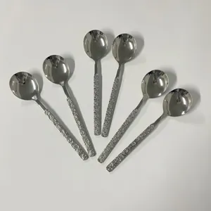 Detail of 6 stainless steel spoons with embossed daisy handles on a white background