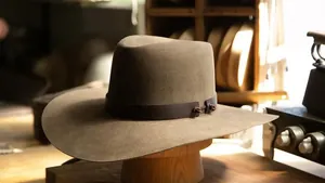 Detalle de sombrero vaquero de fieltro de lana con banda de cuero y nudo en soporte de madera