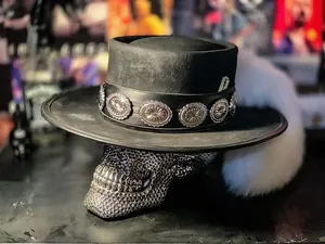 Détail du chapeau en feutre noir avec ruban en cuir à conchos et rasoir décoratif
